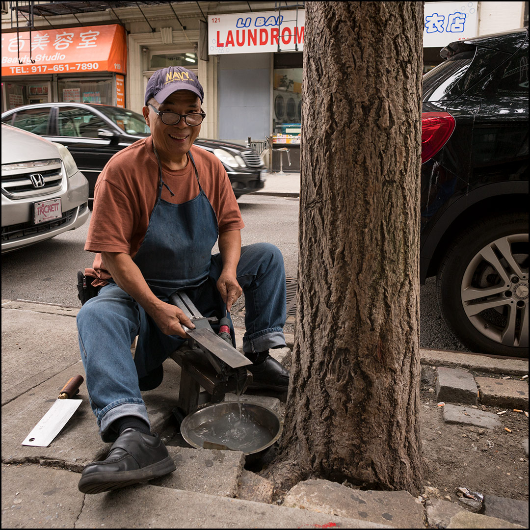 Photo: man sharpening knives sitting on the sidewalk